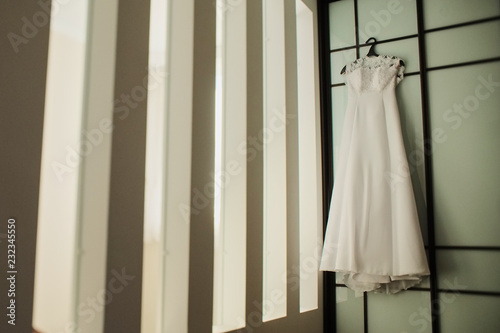 wedding dress on a hanger near the wall. white silk dress, copyspace