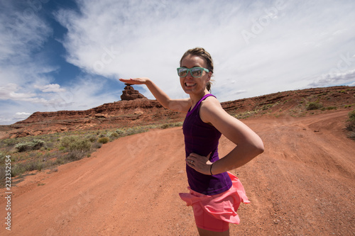 An adult female shows a forced perspective view of Mexican Hat rock formation in the Utah desert by pretending to put her hand on top of the formation