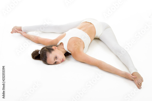 A young woman in a white suit performs acrobatic elements and yoga.