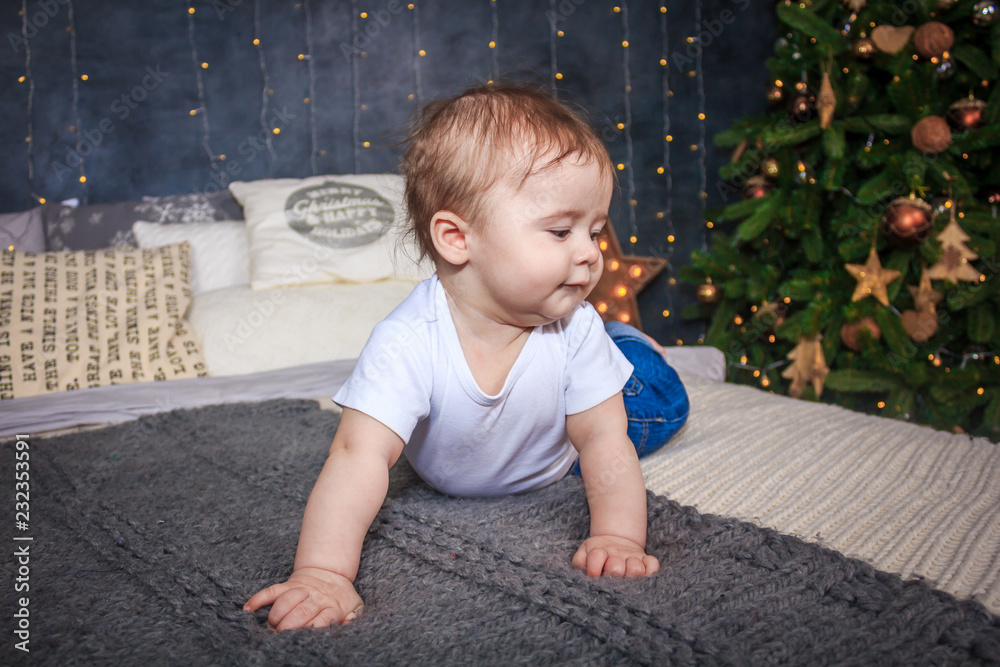 Naklejka premium The little boy is lying on the bed. A big bed and a number of Christmas tree.