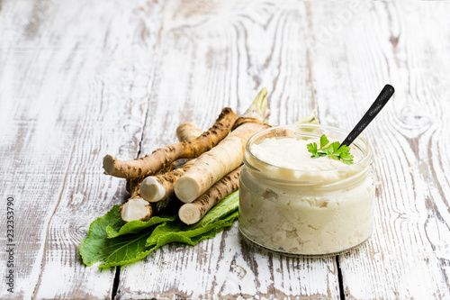 Photo Spicy horseradish sauce in small glass jar on wooden table