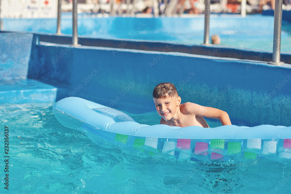 Smiling European boy getting out from water on inflatable mattress in swimming pool at resort.