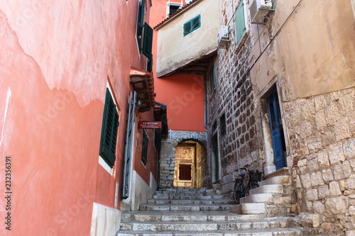 Fototapeta Naklejka Na Ścianę i Meble -  Croatia, Rovinj, August 2018: Adriatic, streets of a small seaside town, sunny hot summer day, old weathered houses, windows with multi-colored shutters, drying clothes on ropes, yachts, blue sea.