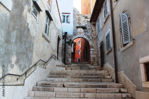 Fototapeta Naklejka Na Ścianę i Meble -  Croatia, Rovinj, August 2018: Adriatic, streets of a small seaside town, sunny hot summer day, old weathered houses, windows with multi-colored shutters, drying clothes on ropes, yachts, blue sea.