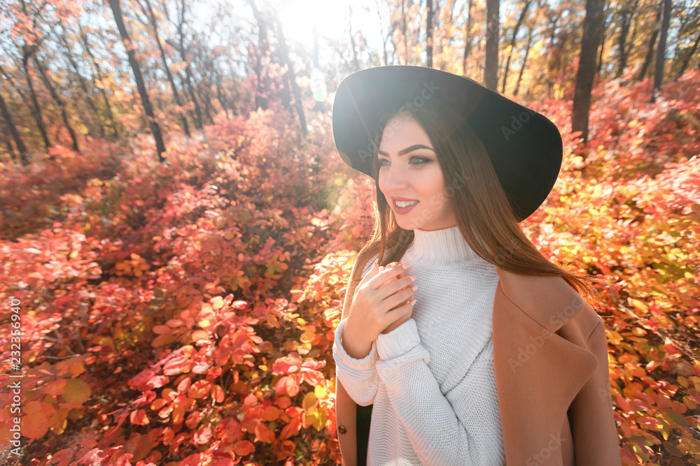 woman in black hat on background of autumn leaves.
