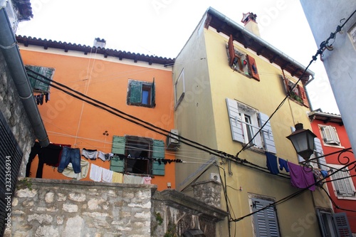Fototapeta Naklejka Na Ścianę i Meble -  Croatia, Rovinj, August 2018: Adriatic, streets of a small seaside town, sunny hot summer day, old weathered houses, windows with multi-colored shutters, drying clothes on ropes, yachts, blue sea.
