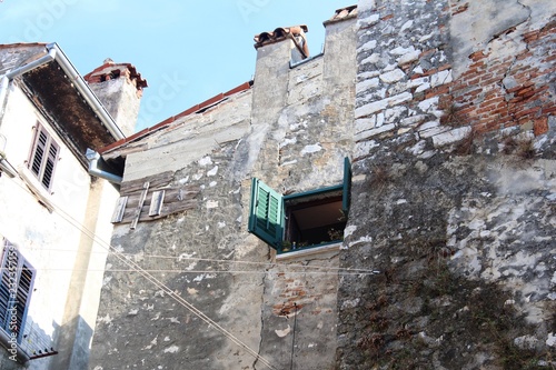 Fototapeta Naklejka Na Ścianę i Meble -  Croatia, Rovinj, August 2018: Adriatic, streets of a small seaside town, sunny hot summer day, old weathered houses, windows with multi-colored shutters, drying clothes on ropes, yachts, blue sea.