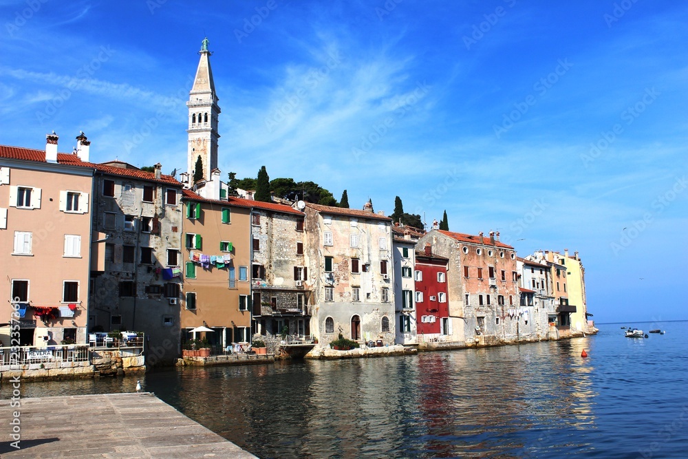Croatia, Rovinj, August 2018: Adriatic, streets of a small seaside town, sunny hot summer day, old weathered houses, windows with multi-colored shutters, drying clothes on ropes, yachts, blue sea.