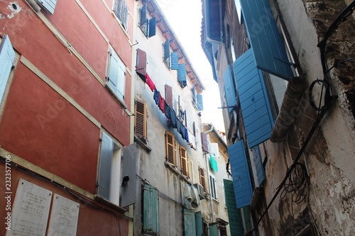 Fototapeta Naklejka Na Ścianę i Meble -  Croatia, Rovinj, August 2018: Adriatic, streets of a small seaside town, sunny hot summer day, old weathered houses, windows with multi-colored shutters, drying clothes on ropes, yachts, blue sea.