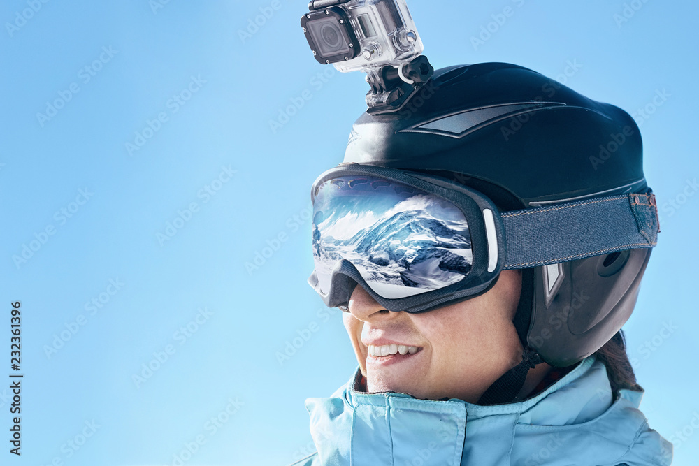 Skier with action camera on a helmet. Ski goggles with the reflection of  snowed mountains. Portrait
