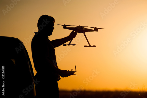 A man holds a flying drone in his hands against the setting sun. 