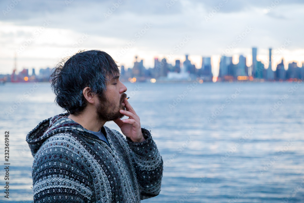 A young man smoking a joint with downtown Vancouver, BC, in the background shortly after Canadian marijuana legalization.