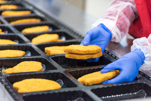 The worker in the factory places the chicken schnitzel photo