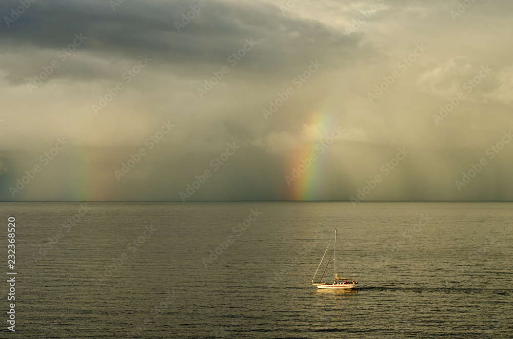 Sailboat in the Atlantic Ocean close to Gran Canaria in a cloudy scene with two rainbows during sunrise Sailboat in the Atlantic Ocean close to Gran Canaria in a cloudy scene with two rainbows during sunrise