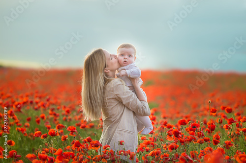 Happy motherhood. Mom and son daughter are playing in the field of flowering red poppies