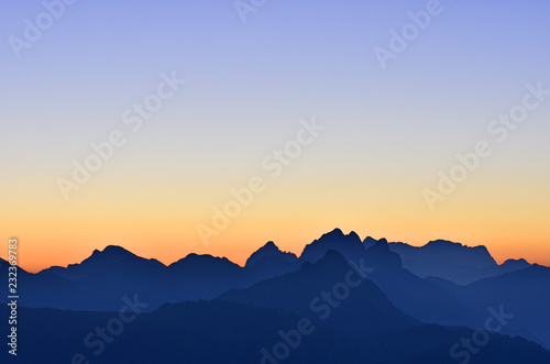 Beautiful morning mood in the Allgaeu Alps at the border region of Germany and Austria. Blue silhouettes of mountain ranges at dawn with orange and blue sky. Zugspitze in the background. Copy space.
