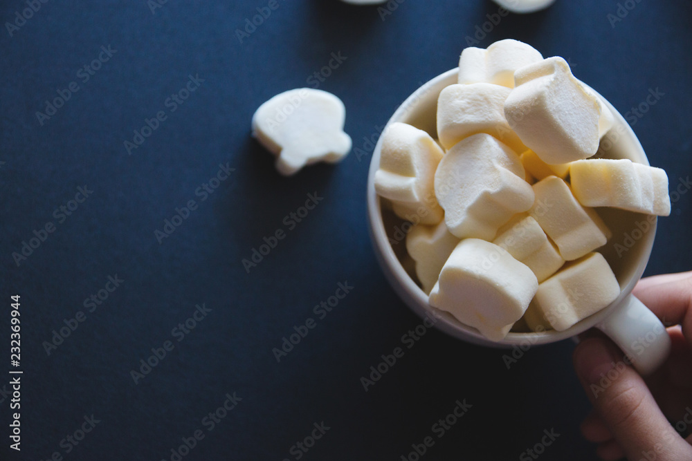marshmallow in the form of bears in a white cup holds a hand on a dark background marshmallow in the form of bears in a white cup holds a hand on a dark background