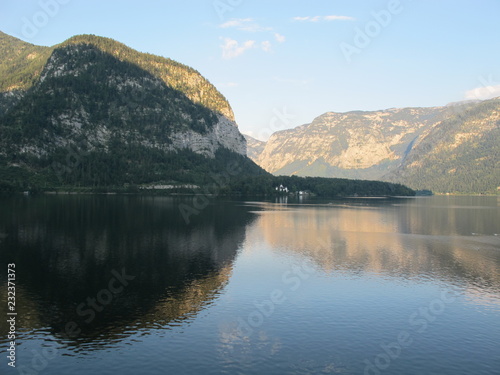 The incredible mountains of Obertraun  reflected on each other  seen from Hallstatt riverside on a sunny and quiet summer afternoon. Austria