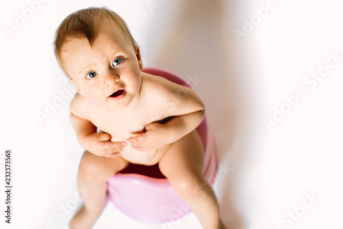 Naked baby sitting on an pink pot for girls