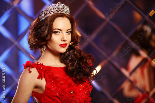Woman queen princess in crown and lux dress. Luxury girl Long shiny healthy volume hair. Waves Curls Updo Hairstyle. Salon Fashion model luxurious vintage interior. Jewelry Earrings