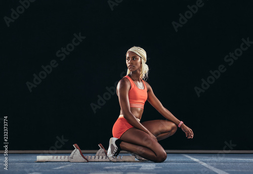 Woman sprinter sitting at the start line on a running track