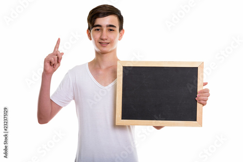 Studio shot of young happy Persian teenage boy smiling while hol