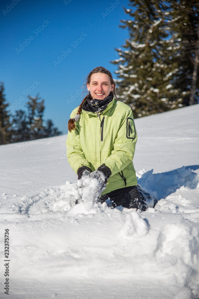 Young beautiful woman playing in snow in green jacket