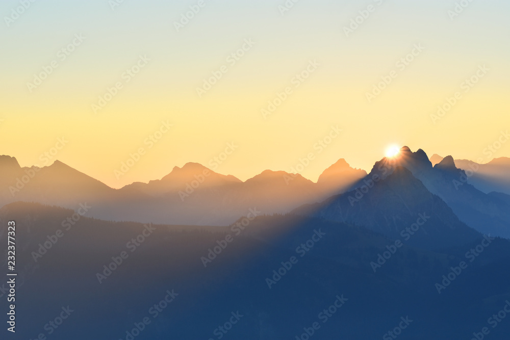 Colorful sunrise over the mountains in the Allgaeu Alps at the border region of Germany and Austria. Silhouettes of mountain ranges with yellow sky. Zugspitze in the background. Copy space.