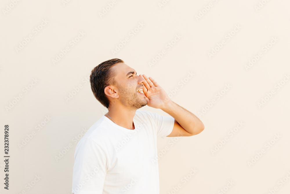 Young man putting hand around mouth yelling loudly on someone far on orange background. Young man putting hand around mouth yelling loudly on someone far on orange background.