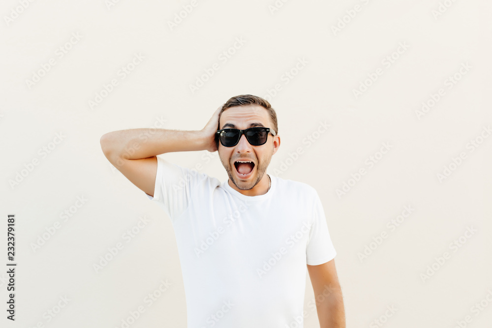 Portrait of a shocked scream young casual man in sunglasses standing isolated over orange background,