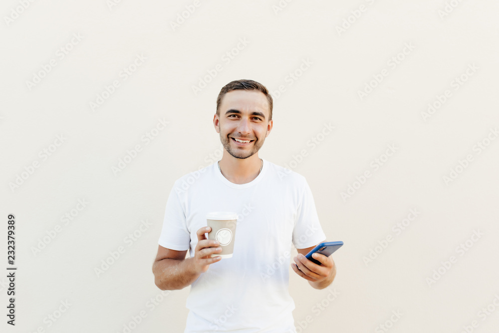Young handsom man in casual wear checking news on smartphone while holding takeaway coffee, isolated on pastel background Young handsom man in casual wear checking news on smartphone while holding takeaway coffee, isolated on pastel background