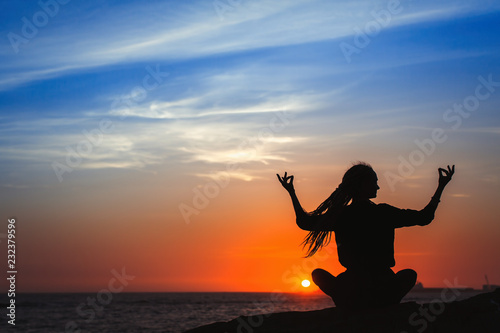 Yoga woman silhouette series. Meditation on the ocean during amazing sunset.