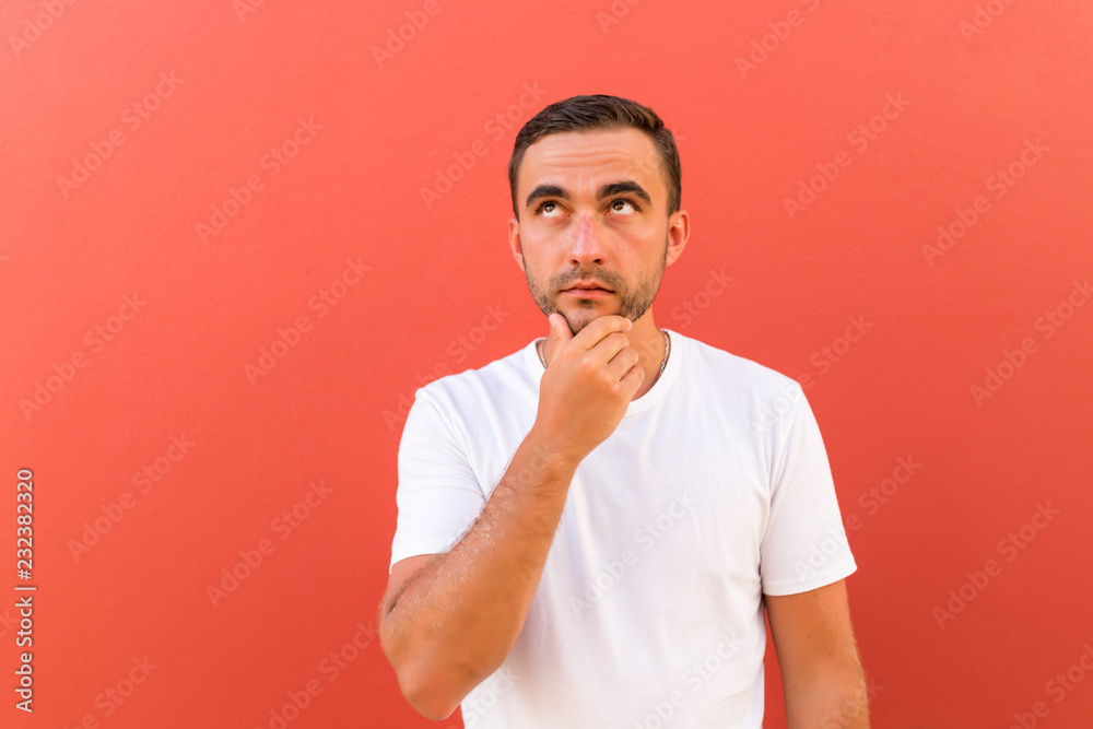 Portrait of young man holding hand up to chin with arms folded isolated on red background
