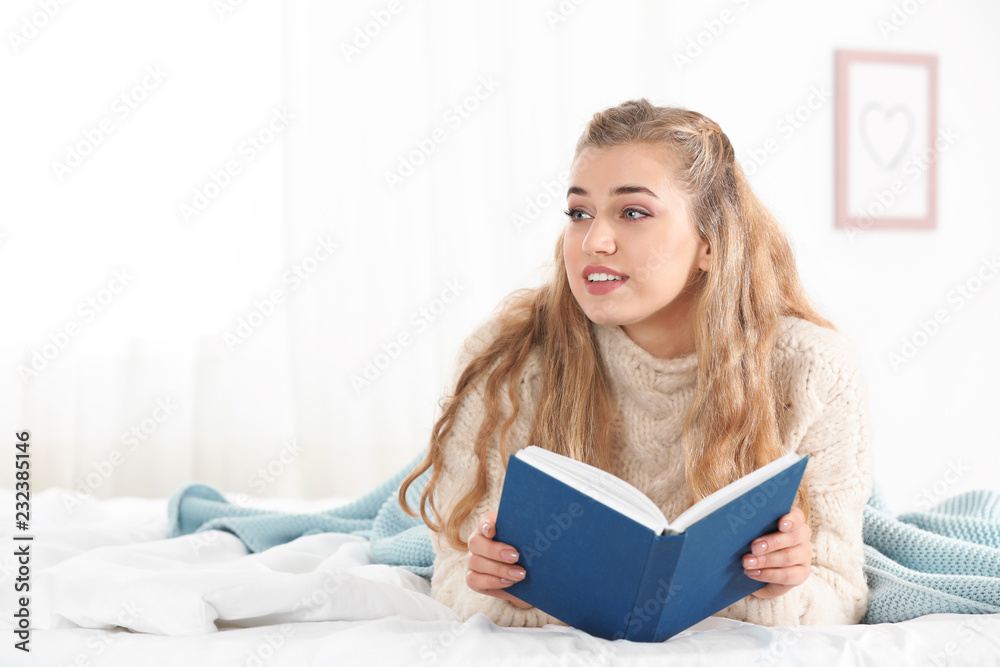 Attractive young woman in cozy warm sweater reading book on bed at home. Space for text Attractive young woman in cozy warm sweater reading book on bed at home. Space for text