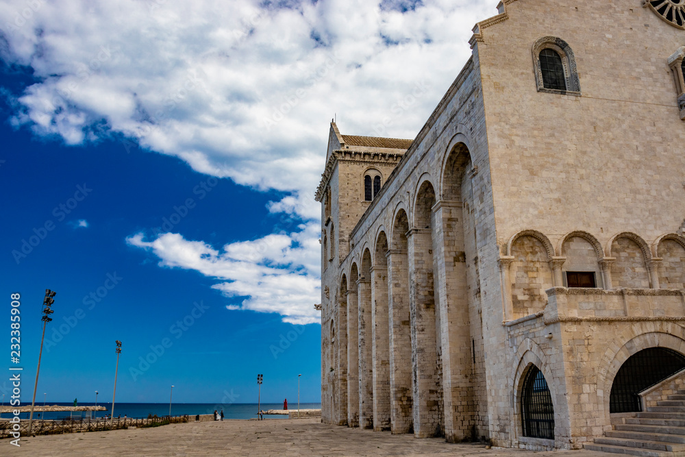 Fototapeta premium The beautiful Romanesque Cathedral Basilica of San Nicola Pellegrino, in Trani. Construction in limestone tuff stone, pink and white. A pointed arch under the bell tower. Italy, Puglia, Bari, Barletta