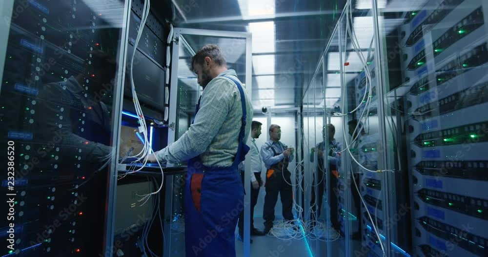 Wide shot of a male technicians working in a data center carrying cable down the corridor amongst rows of server racks