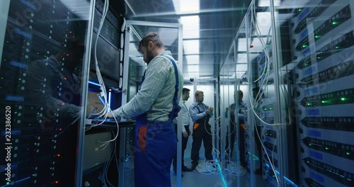 Wide shot of a male technicians working in a data center carrying cable down the corridor amongst rows of server racks