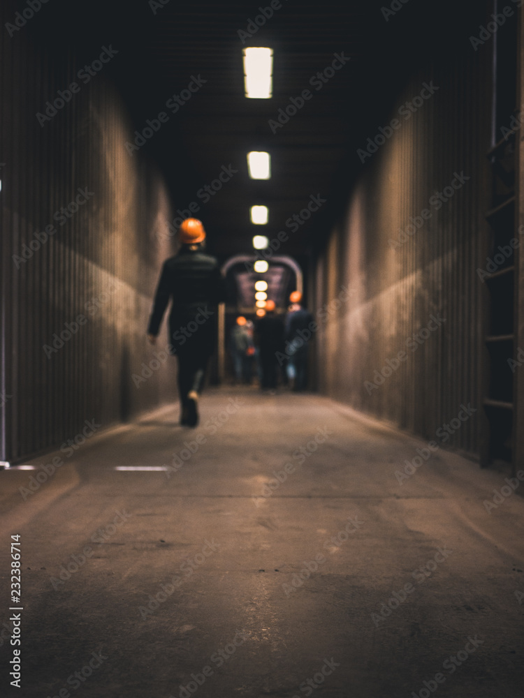 hallway in a factory with neon lights shining and workers walking out of focus