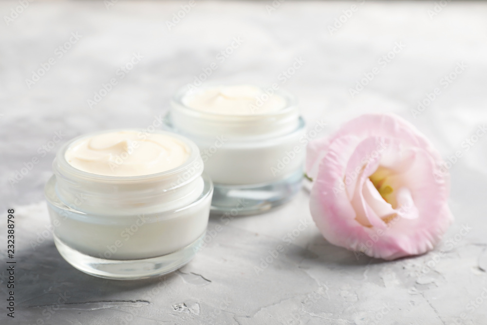 Closeup view of hand cream jars with flower on gray background Closeup view of hand cream jars with flower on gray background