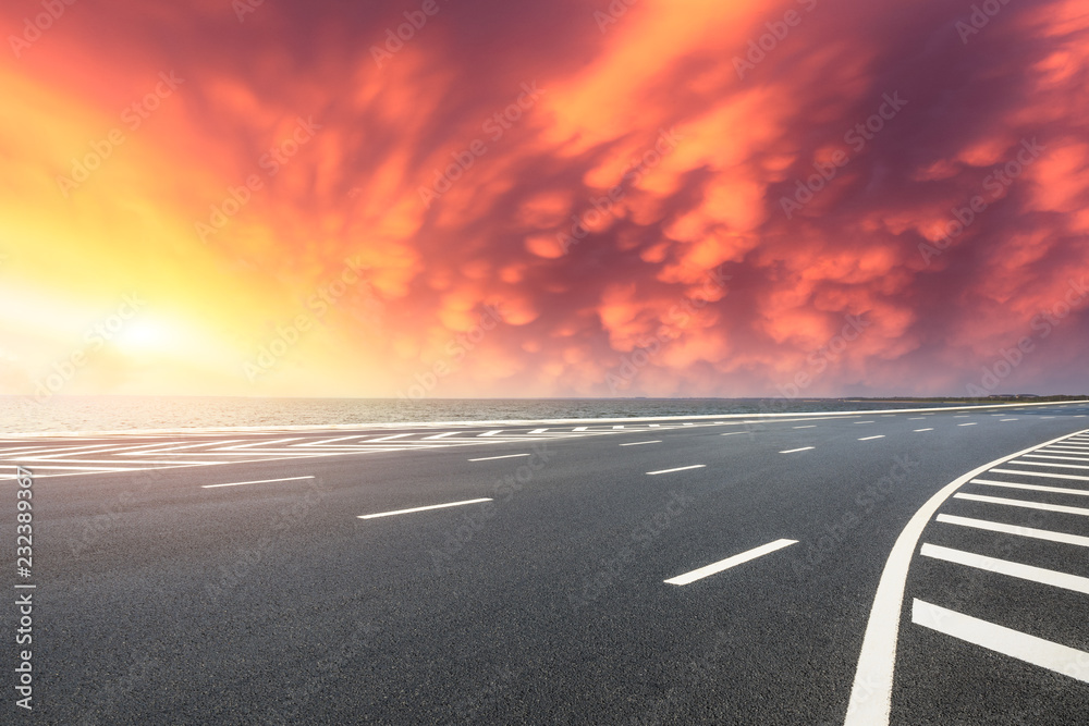 Fototapeta premium Asphalt road and dramatic sky with coastline at sunset