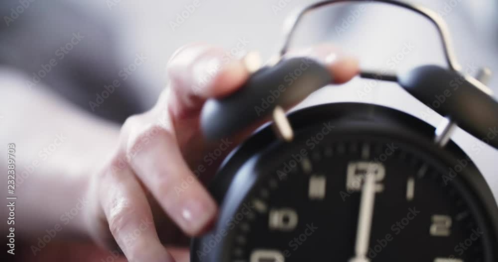 A sleepy woman turns over or snoozes an alarm clock and rolls back in bed.