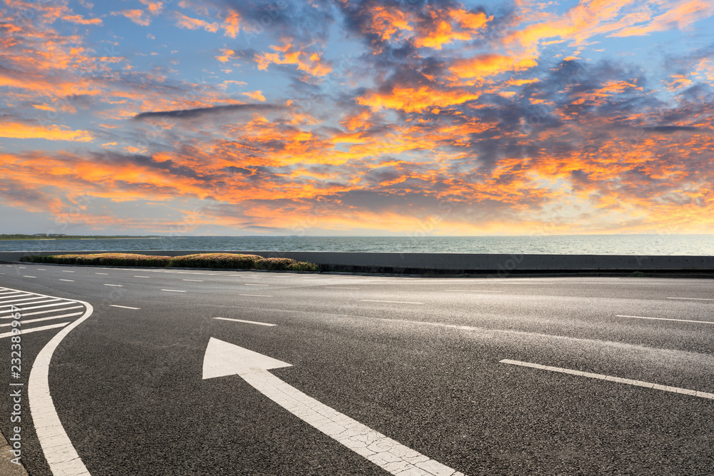 Fototapeta premium Asphalt road and dramatic sky with coastline at sunset