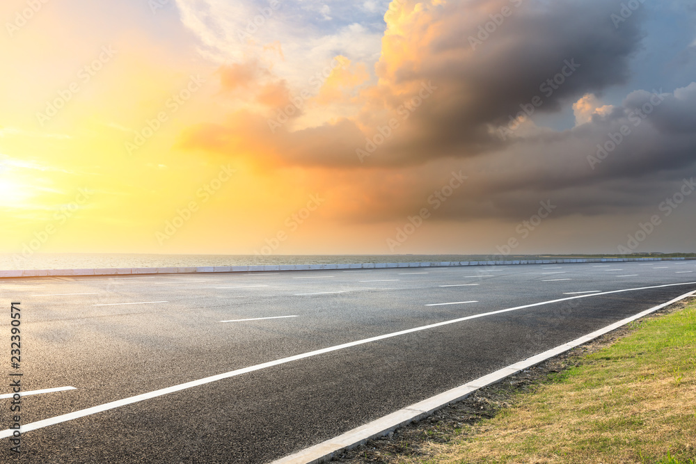 Asphalt road and dramatic sky with coastline at sunset