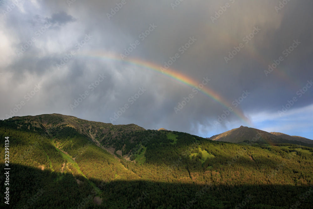 Bright Rainbow in the sky above Kanas Nature Reserve. Xinjiang Province, China. Clouds, alpine high altitude forest and fresh air. Altai Mountains near the border of, Kazakhstan, Russia and Mongolia.