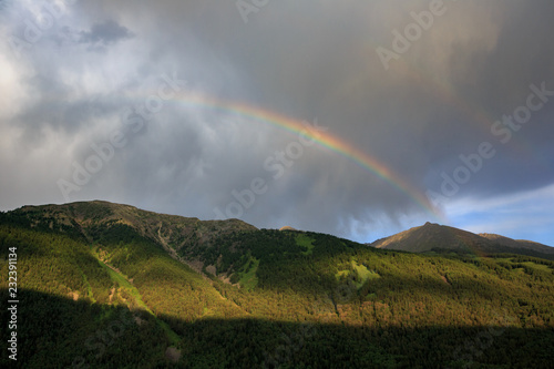 Bright Rainbow in the sky above Kanas Nature Reserve. Xinjiang Province, China. Clouds, alpine high altitude forest and fresh air. Altai Mountains near the border of, Kazakhstan, Russia and Mongolia.