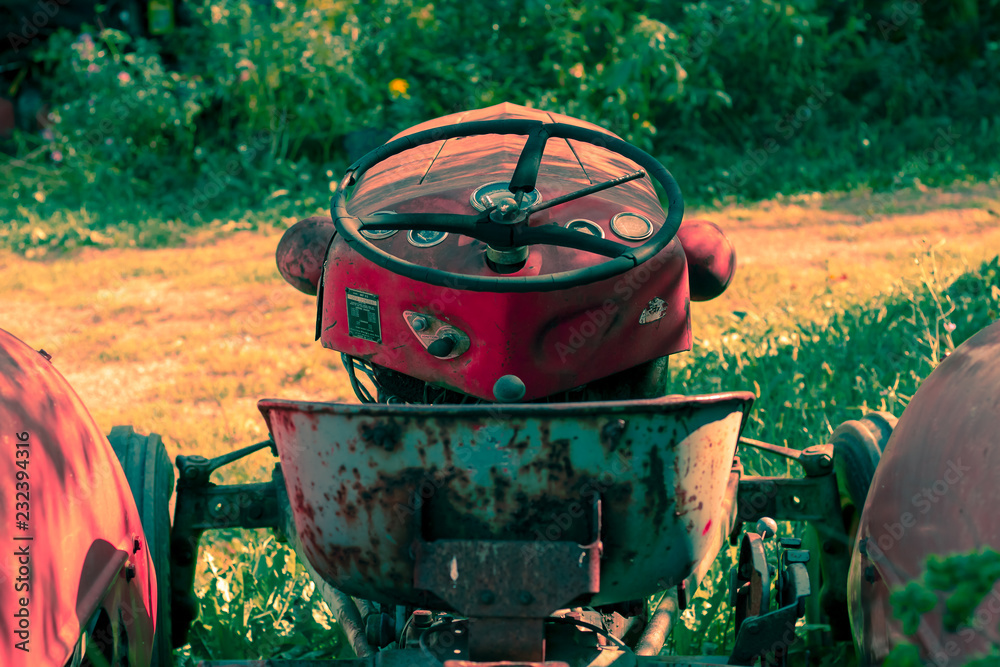 Little red tractor on a sunny fall day sitting in tall grass.