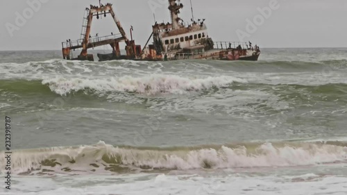 Tilt up revealing eerie shipwreck along Namibia Skeleton Coast on overcast day photo