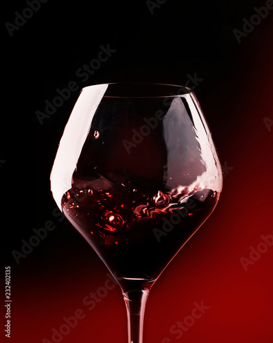 Red wine, splash in a glass, dry cabernet sauvignon, dark red background, defocused in motion image, shallow depth of field