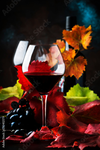 Dry red wine from pinot noir grapes in large glasses, autumn still life with red and yellow leaves on dark background, low key, selective focus