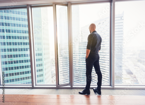 Young attractive stylish bald man in a business suit in his office in a skyscraper, business, finance, success